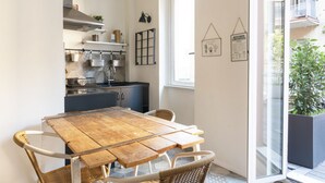 A compact kitchen with a wooden table and wicker chairs, a window with a view of a balcony, and kitchen decor including a hanging light and framed pictures. - Happy Travelers Apartment (Como)