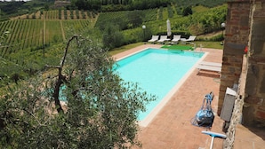 Piscina com vista para vinhedos e colinas ao fundo.