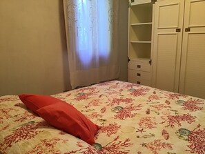 Makuuhuoneessa on sänky, punainen tyyny, kukkakuviollinen päiväpeite, vaatekaappi ja verho.