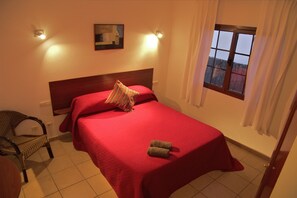 Une chambre à coucher bien rangée, avec un lit simple, une chaise, une petite table et une fenêtre avec des rideaux.
