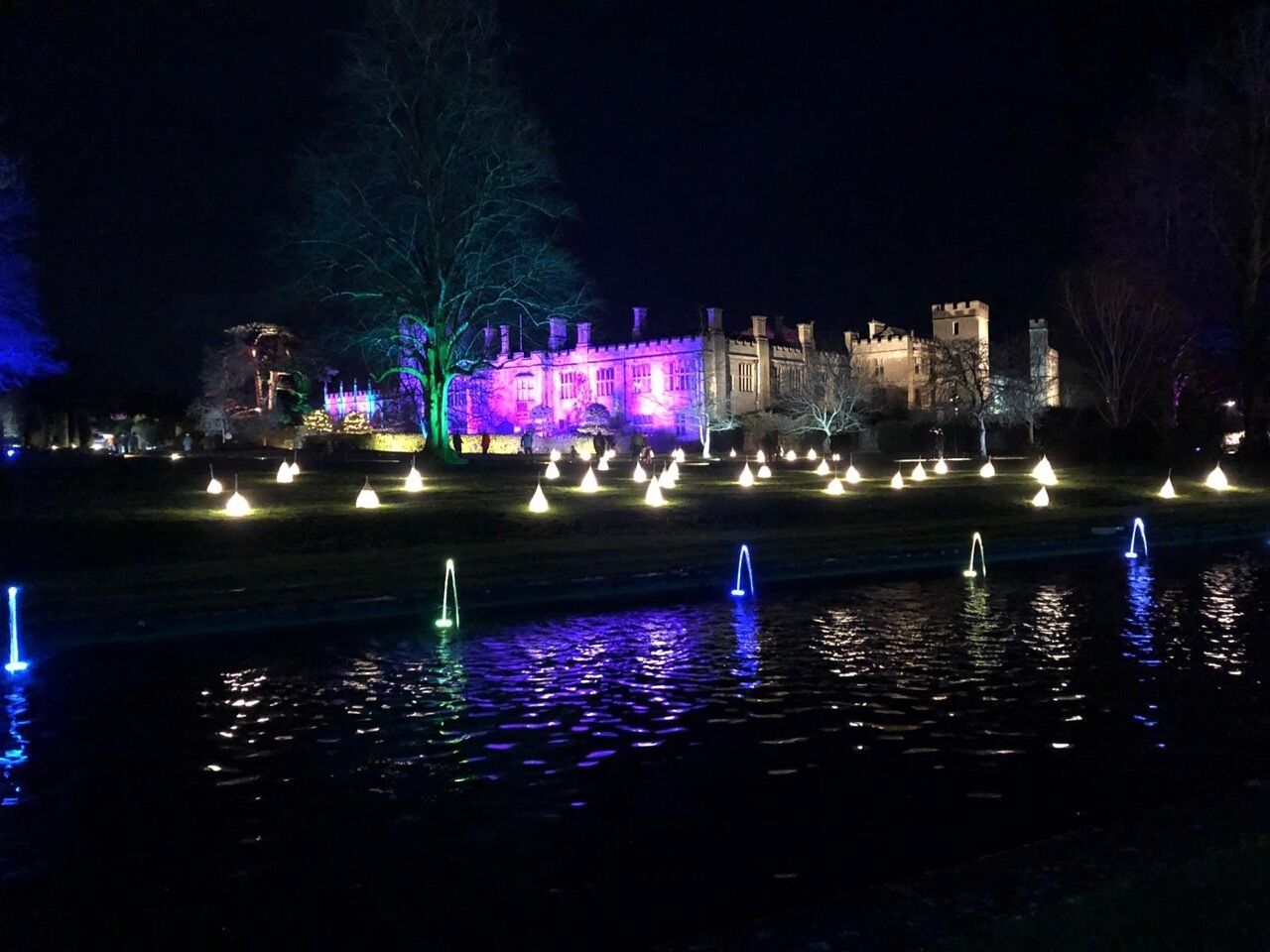 Un edificio con apariencia de castillo y fuentes iluminadas, en un entorno nocturno.