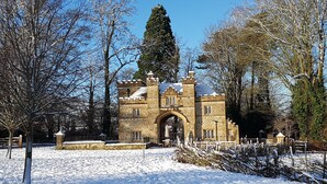 Un edificio histórico de piedra con una amplia entrada abovedada, rodeado de árboles cubiertos de nieve y un cielo azul despejado.