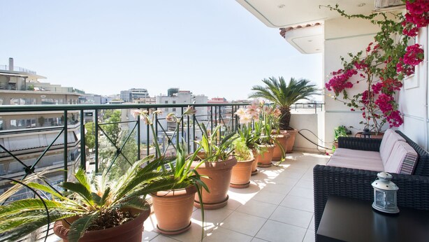 A balcony with potted plants, a wicker sofa, and a lantern. - Acropolis view Penthouse (Athina)