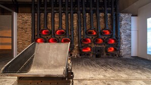 A room with a brick wall, a metal structure with multiple red glowing elements, and a wooden platform. - Acropolis view Penthouse (Athina)