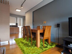 A modern dining area with a wooden table and chairs, a green rug, and a television on a stand.