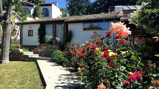 A white building with a tiled roof, a stone pathway, and a garden with various flowers. - Garden House, Ephesus Holiday Rentals (Selçuk)