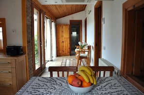 A dining area with a table set for two, a bowl of fruit, and a view of a kitchen and a wooden door.