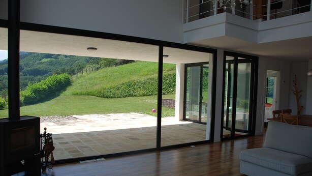 Un salon spacieux doté d’une grande porte-fenêtre coulissante qui donne sur un patio offrant une vue sur une colline verdoyante.
