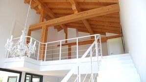 Un plafond en bois avec des poutres apparentes, un escalier blanc et un lustre.