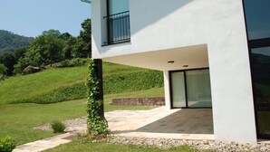 Une maison moderne à deux étages, dotée d’un balcon, d’un chemin en pierre et entourée d’un paysage verdoyant luxuriant.