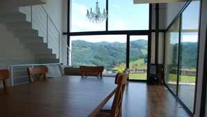 Un vaste espace dédié à la salle à manger, avec une grande table et des chaises en bois, un escalier et une vue sur un paysage montagneux grâce à de grandes fenêtres.