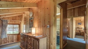 Ein Interieur einer Holzhütte mit einem Holzschrank, einem Fenster mit Vorhängen und einer Tür zu einem anderen Raum.