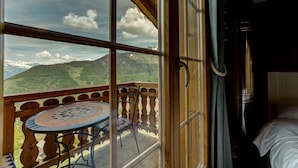 Ein Zimmer mit Holzbalkon, einem runden Tisch und Blick auf schneebedeckte Berge.