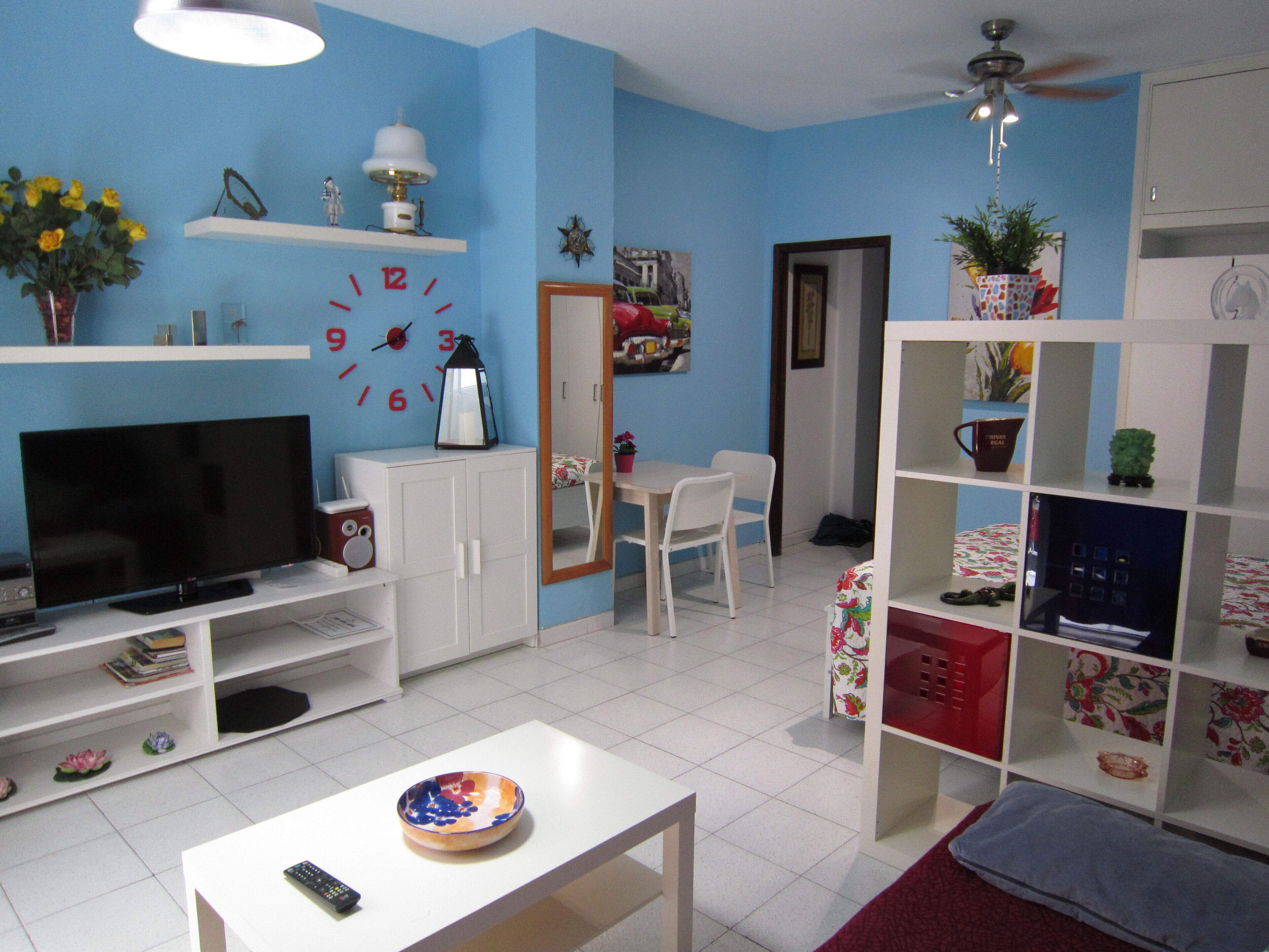 A living room with a TV, white cabinets, a dining table, and a bookshelf.