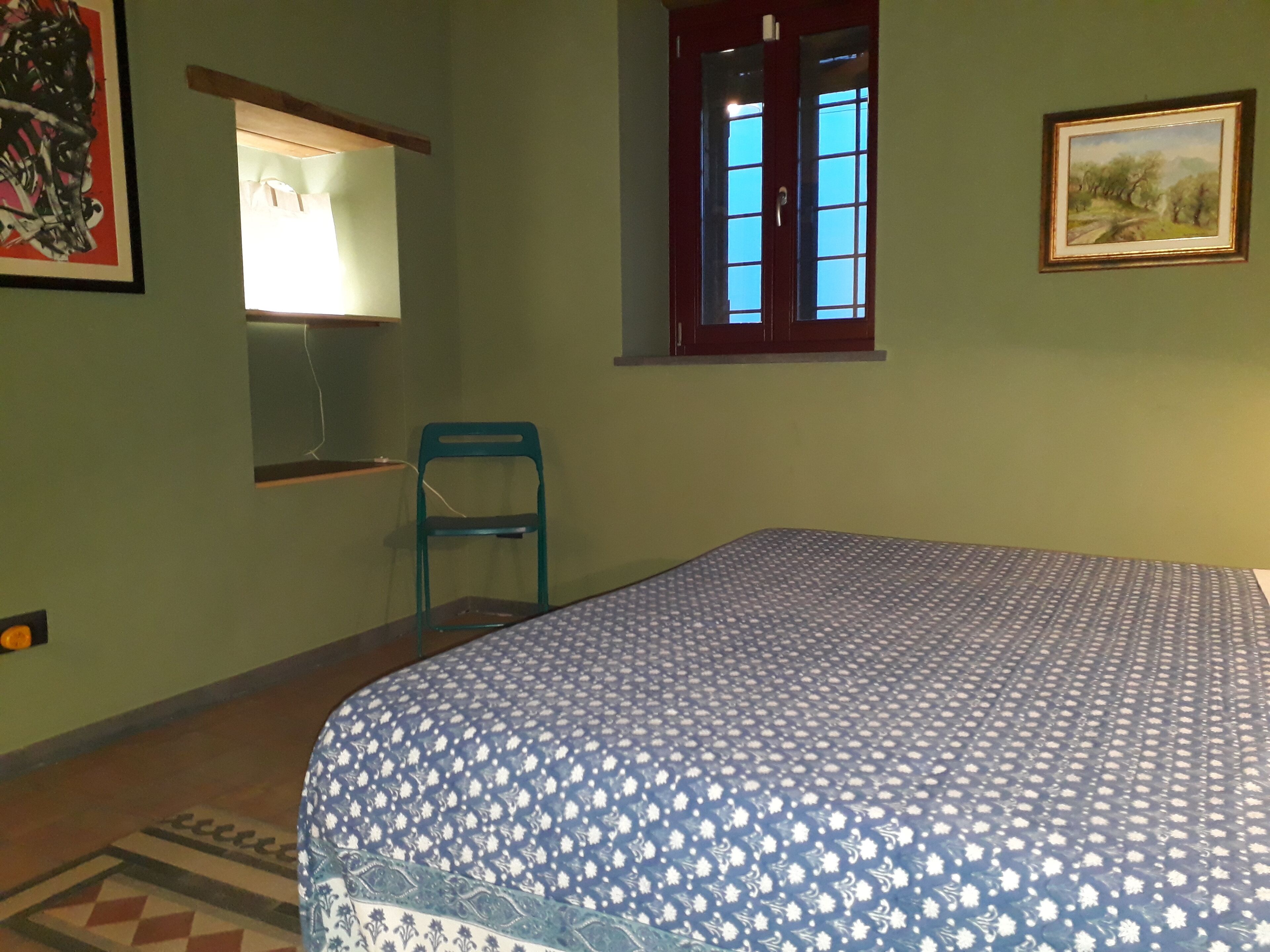 Ein Zimmer mit einem Bett, einem Sessel, einem Fenster und einem Bild an der Wand.