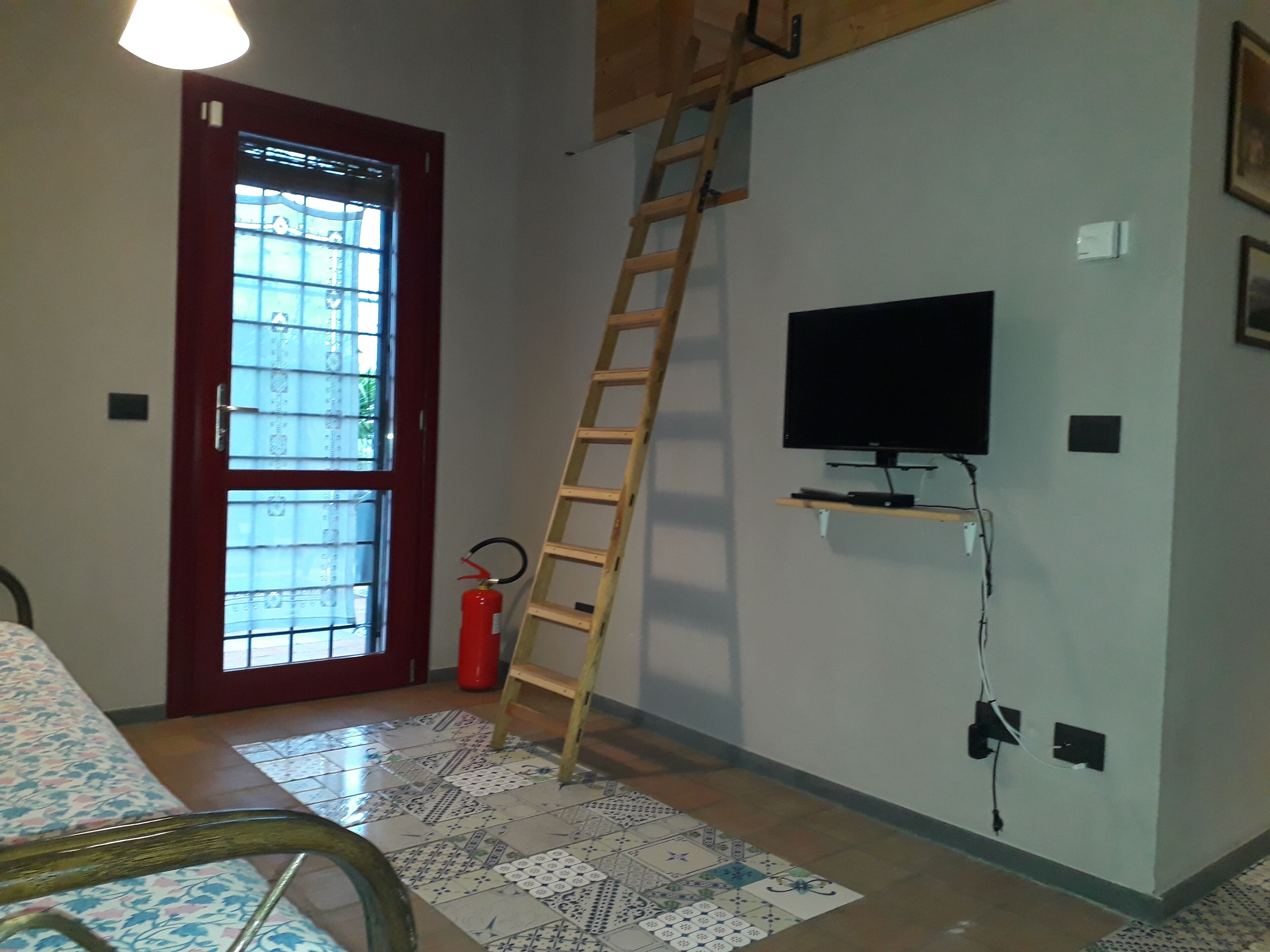 A room with a wooden ladder, a television mounted on the wall, a fire extinguisher, and a patterned rug.