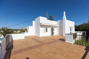 Um edifício branco com um pátio ladrilhado, uma chaminé e uma pequena área de piscina.