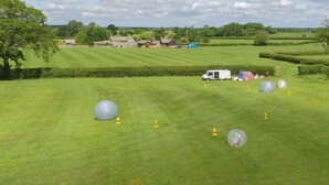 A grassy field with large transparent balls and yellow cones, likely for a recreational activity. - The Cotswold Manor Vineyard, Exclusive Hot Tub, Games Barn, 70 acres of Parkland (Bampton)