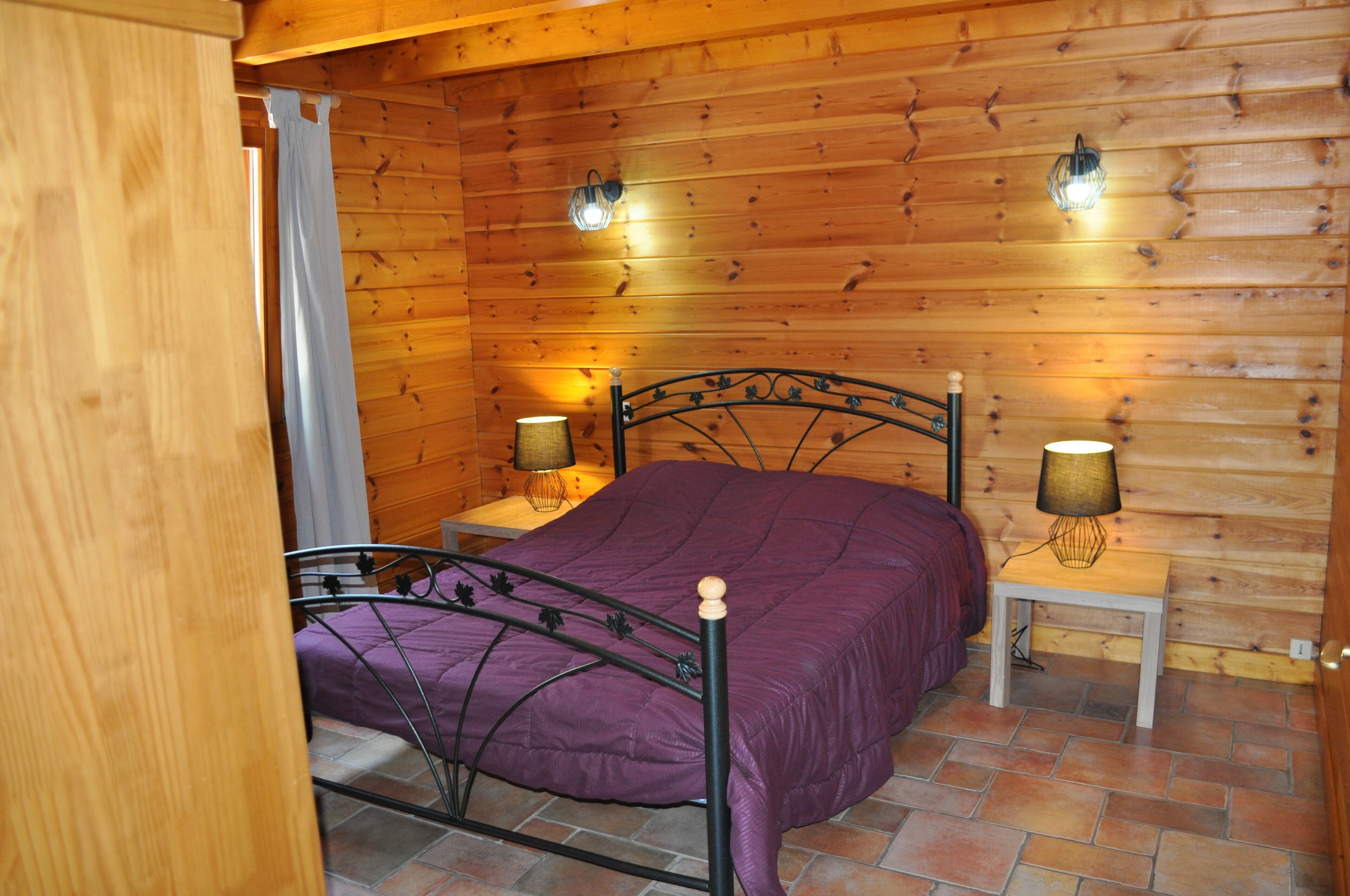 Une chambre dans une cabane en bois, avec un lit, deux lampes de chevet et une porte en bois.