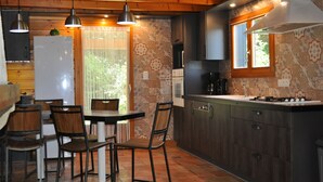 Une cuisine avec des meubles de rangement en bois, une table à manger avec des chaises et des luminaires suspendus.