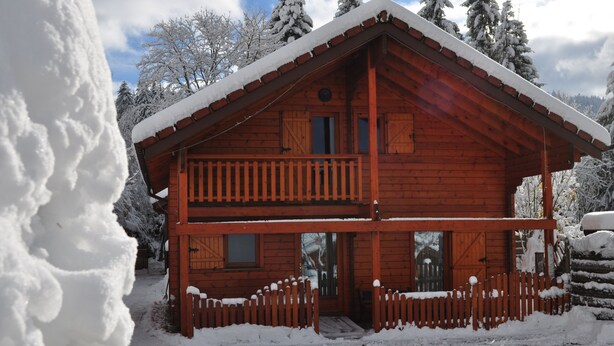 Une cabane en bois dotée d’un balcon, entourée d’arbres couverts de neige.