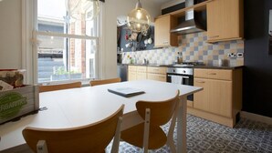 Een keuken met een witte tafel, houten stoelen, hangende lampen en een betegelde achterwand.