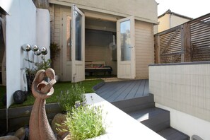 Una casa moderna amb façana de fusta, un petit jardí amb una escultura i una porta que dona a una zona exterior coberta.