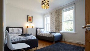 Een slaapkamer met twee bedden, een bureau, een stoel, een groot raam en een plafondlamp.