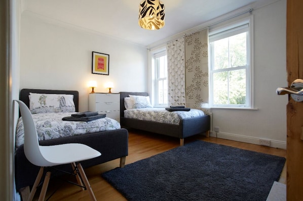 A bedroom with two beds, a desk, a chair, a large window, and a ceiling light fixture.
