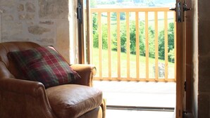 Una habitación con un sofá de cuero marrón, un cojín de cuadros y una puerta de madera que da a una terraza de madera con vistas a la vegetación.