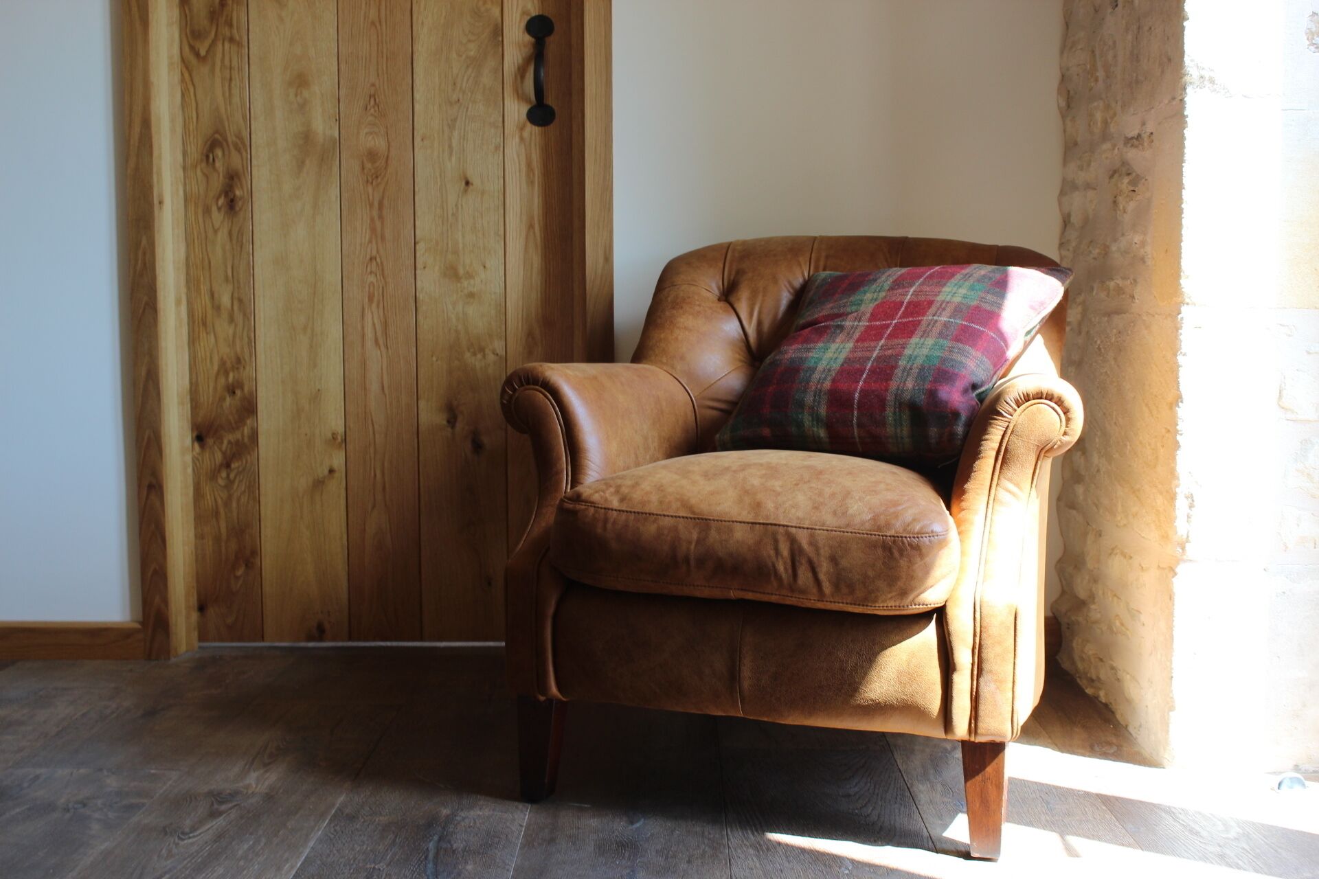 Un sillón de cuero marrón con un cojín de cuadros en una habitación con paredes de madera y una pared de acento de piedra.