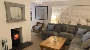 Un salon chaleureux avec une cheminée, un canapé, une table basse et un fauteuil en osier.
