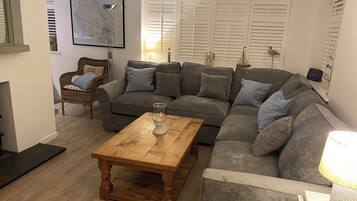 Un salón con un sofá seccional gris, una mesa de centro de madera, un sillón de mimbre y un mapa en la pared.