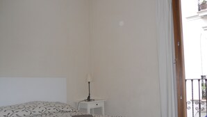 Et soveværelse med seng, et natbord, en lampe og udsigt til den udendørs balkon.