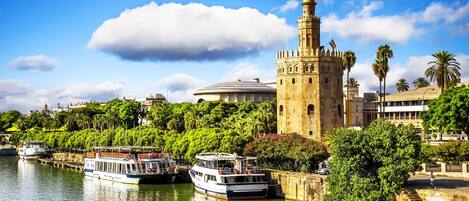 A historic tower, a river with boats, and lush greenery along the waterfront.