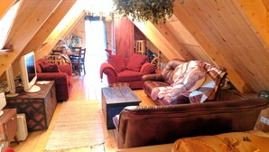 Une pièce mansardée chaleureuse, avec un plancher en bois, un canapé en cuir, un fauteuil rouge et un bureau avec un ordinateur.