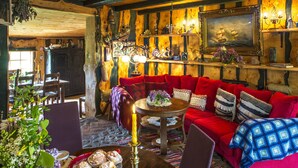 Une pièce chaleureuse avec un plafond en bois, un canapé rouge, une table en bois sur laquelle est posée une bougie, et un tableau accroché au mur.