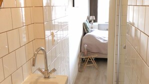 A narrow bathroom with a sink and a mirror, leading to a bedroom with a bed and a nightstand. - Lovely spacious, luxurious apartment with canal view (Amsterdam)