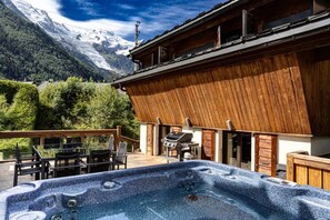 Una cabaña de madera con jacuzzi, mobiliario exterior y vistas a la montaña.