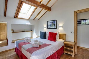A bedroom with a bed, a skylight, a painting, and a wooden wardrobe.