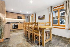 A modern kitchen with wooden cabinets, a dining table with chairs, and a large window with curtains.