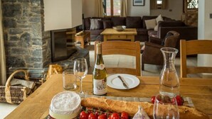 A dining table set with a bottle of wine, a glass, a plate, a cheese wheel, a baguette, cherry tomatoes, and a garlic bulb. - Chalet Grand Cru Central 5 Bed with Jacuzzi (Chamonix-Mont-Blanc)