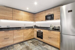A modern kitchen with wooden cabinets, a stainless steel refrigerator, a microwave, and a built-in oven. - Chalet Grand Cru Central 5 Bed with Jacuzzi (Chamonix-Mont-Blanc)