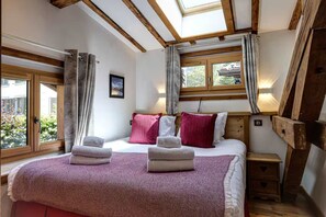 A bedroom with a bed, pillows, a bedside table, a nightstand, and a window with curtains. - Chalet Grand Cru Central 5 Bed with Jacuzzi (Chamonix-Mont-Blanc)