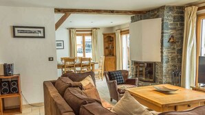 A cozy living room with a brown leather sofa, wooden dining table, and a stone fireplace. - Chalet Grand Cru Central 5 Bed with Jacuzzi (Chamonix-Mont-Blanc)