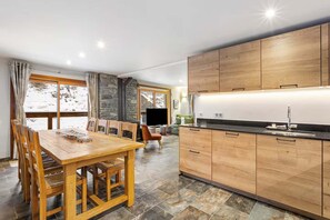 Une cuisine moderne avec des meubles en bois, un coin repas avec une table et des chaises en bois, et un mur en pierre.