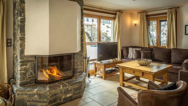 A cozy living room with a stone fireplace, a comfortable sofa, and a television. - Chalet Grand Cru Central 5 Bed with Jacuzzi (Chamonix-Mont-Blanc)