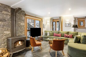 A cozy living room with a stone wall, a fireplace, a green sofa, and a flat-screen TV.