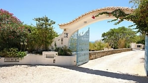Une entrée fermée par un portail, agrémentée d’une arche décorative, un mur blanc portant une inscription et une allée gravillonnée.
