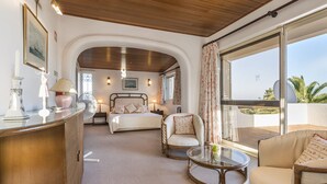 Une chambre d’hôtel avec un lit, deux chaises, une petite table, une vitrine et une grande fenêtre donnant sur un paysage agréable.
